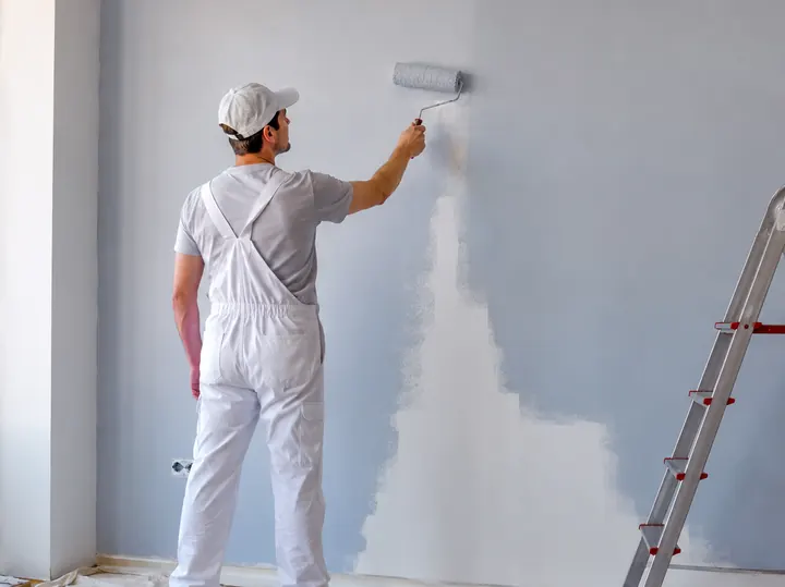 Pintor aplicando tinta na parede com rolo em ambiente interno